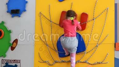 小女孩爬上室内的攀爬墙。 婴儿在操场上玩孩子们`体育游戏